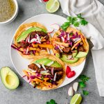 Three ancho chicken tacos with mango slaw, avocado, and radish on a plate