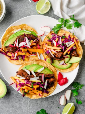 Three ancho chicken tacos with mango slaw, avocado, and radish on a plate