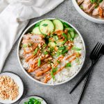 Pork and rice bowl with sliced marinated cucumbers and a creamy peanut sauce, garnished with crushed peanuts and scallions.
