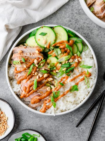 Pork and rice bowl with sliced marinated cucumbers and a creamy peanut sauce, garnished with crushed peanuts and scallions.
