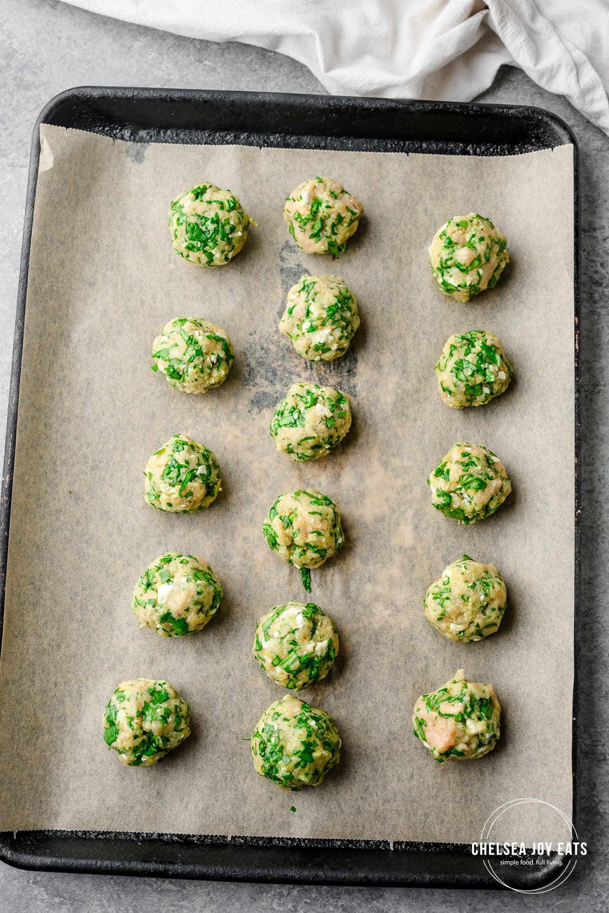Uncooked gluten free chicken meatballs lined up on a baking sheet