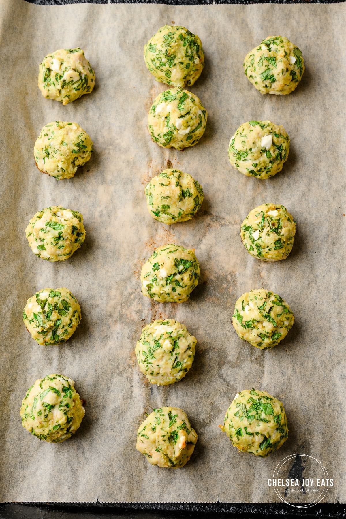 Baked spinach and feta chicken meatballs lined up on a baking sheet