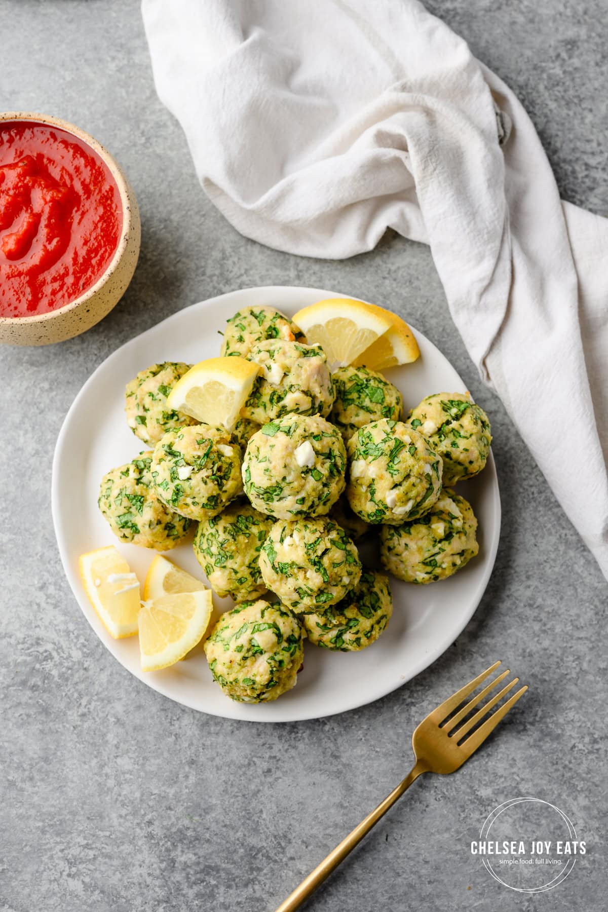 Gluten free spinach and feta chicken meatballs piled on a plate and garnished with lemon wedges