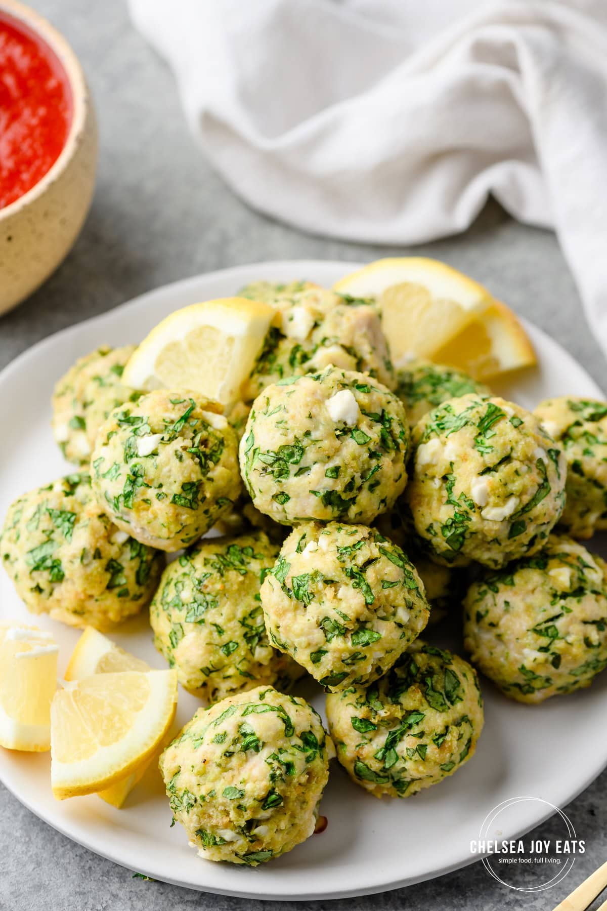 Closeup of gluten free chicken meatballs with spinach and feta cheese piled on a plate and garnished with lemon wedges