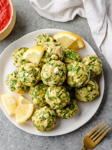 Spinach and Feta Chicken Meatballs piled on a plate and garnished with lemon wedges