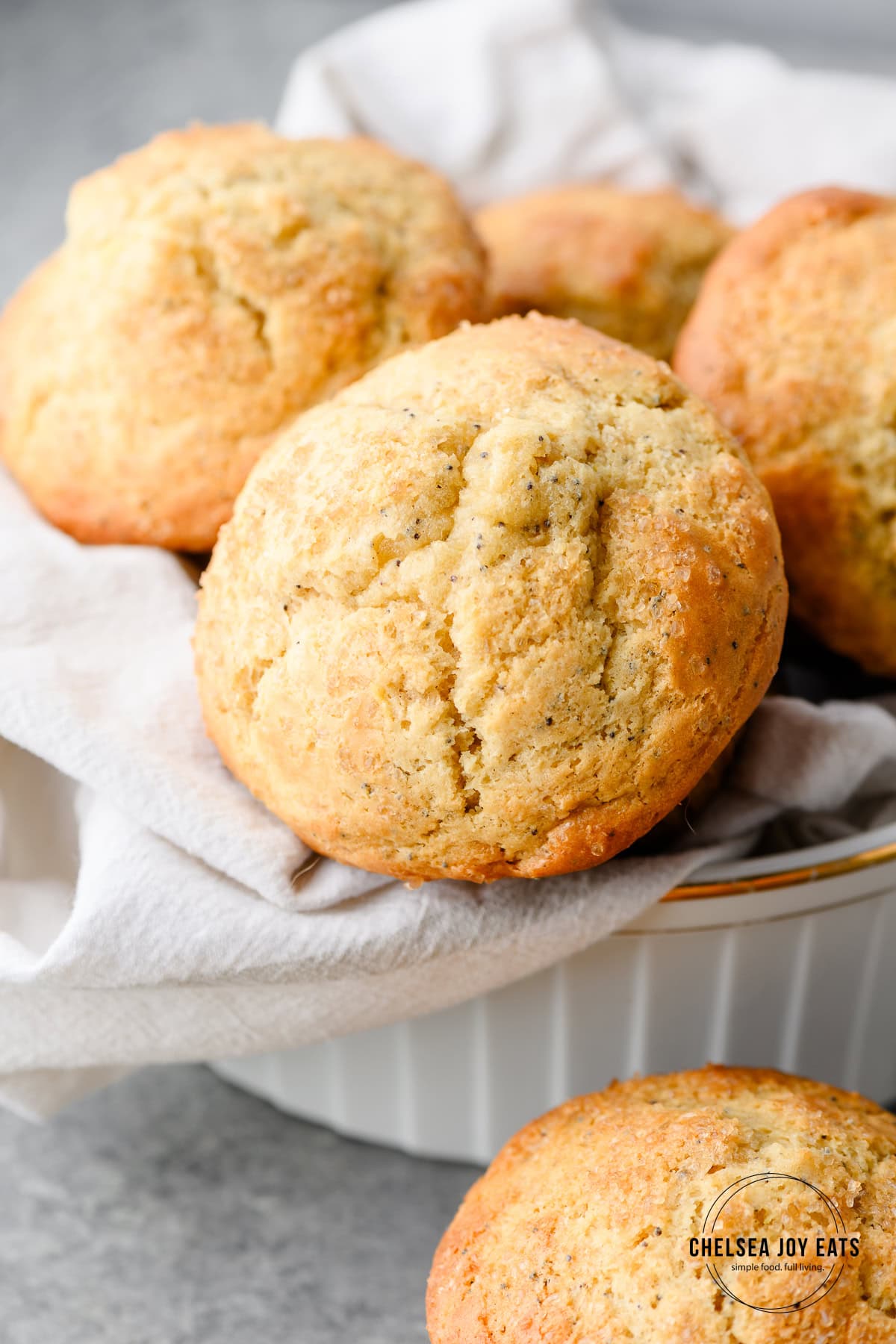 Closeup of the top of a lemon poppyseed muffin, with more muffins in a bowl with it