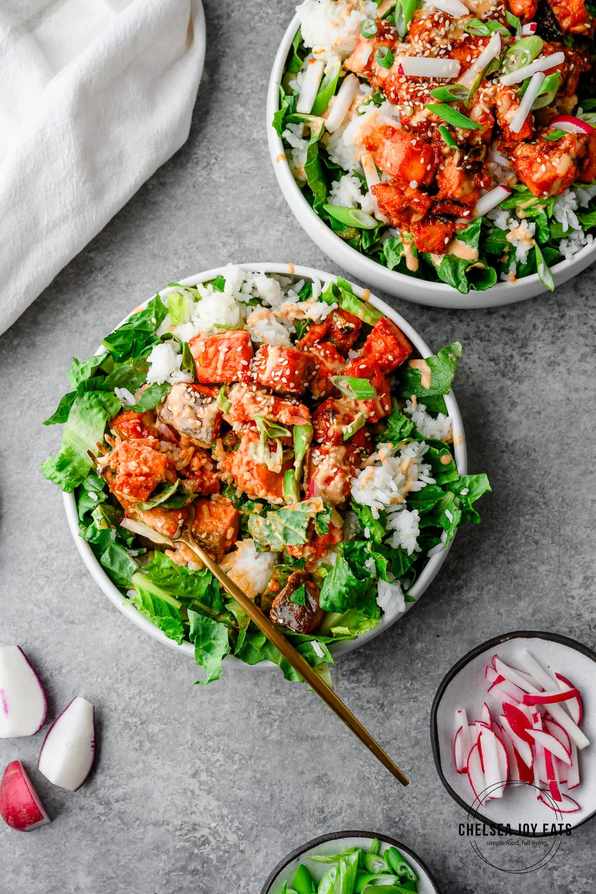 Bowls of spicy gochujang salmon over chopped romaine and rice with a fork scooping a bite