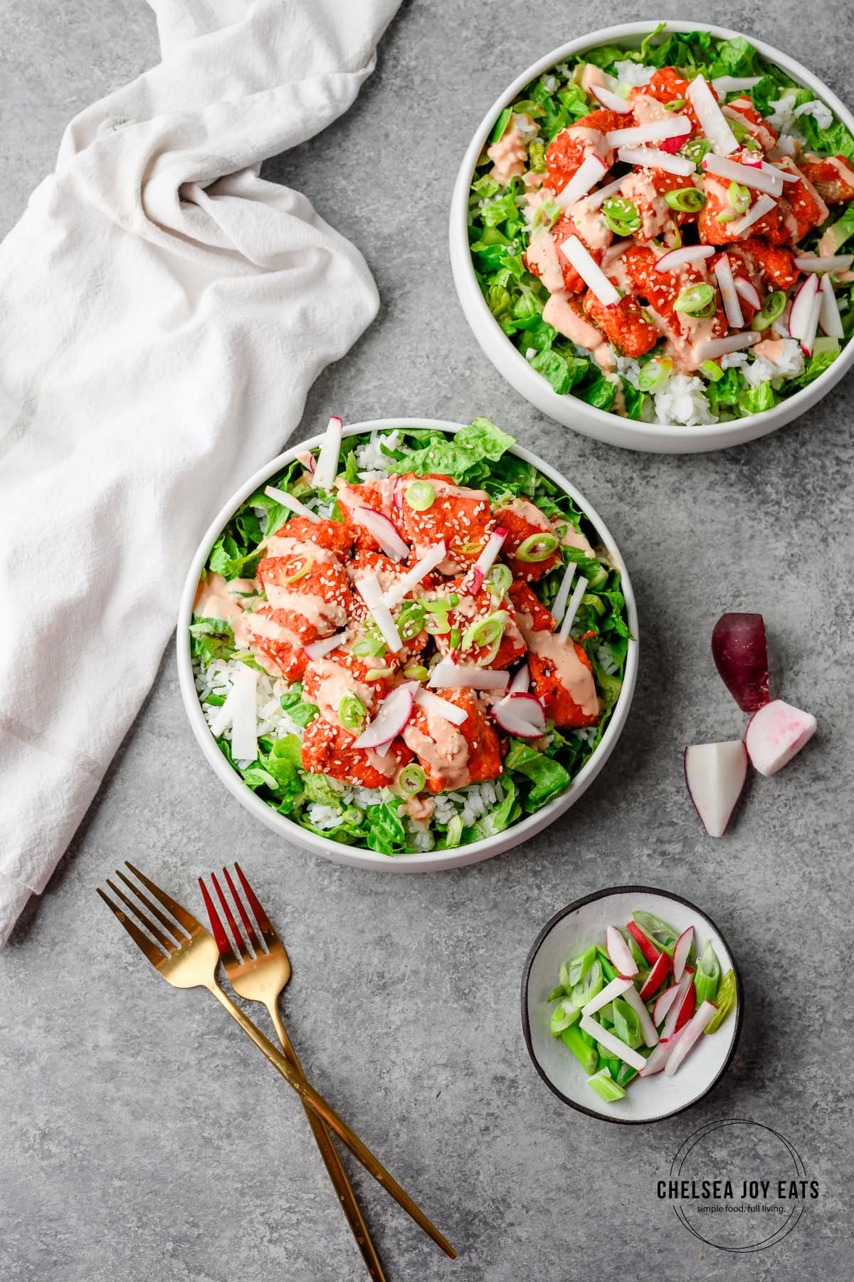 Bowls with gochujang salmon over chopped romaine lettuce and rice, topped with radish and green onions