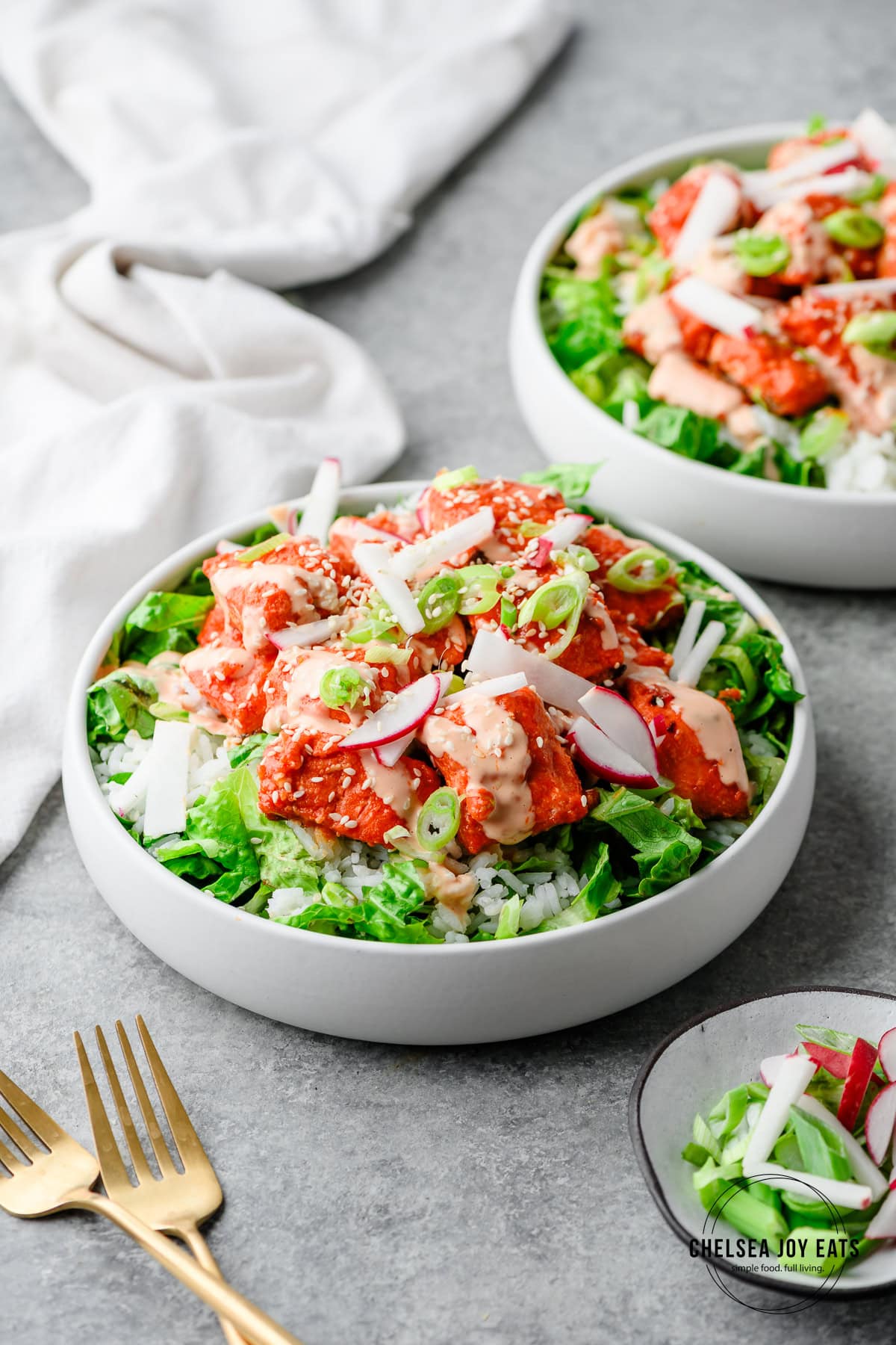 Bowls with chopped romaine and rice topped with spicy gochujang salmon, scallions, radish, and sesame seeds