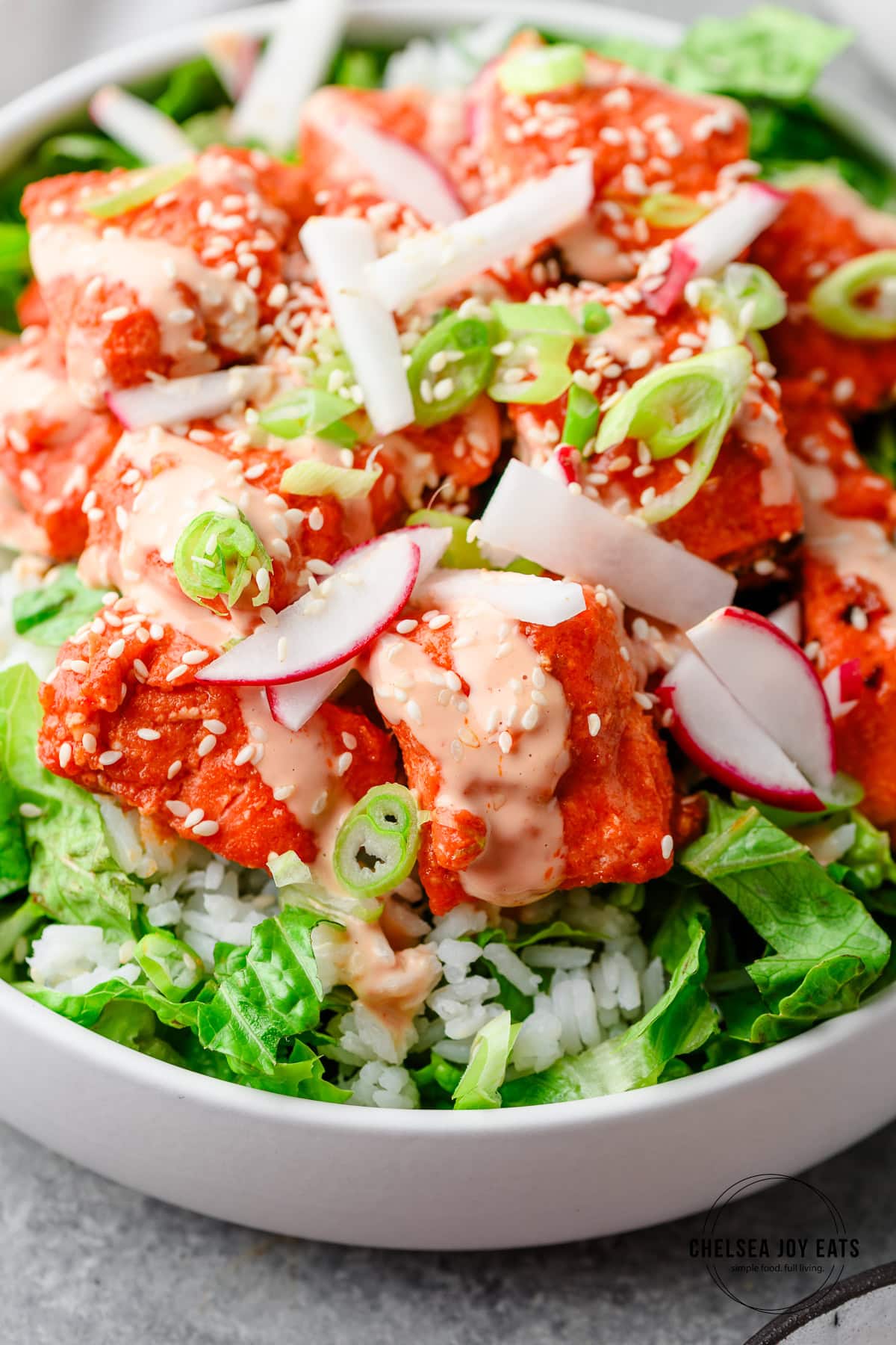 Closeup of gochujang salmon topped with a mayo drizzle, sesame seeds, radish, and green onions
