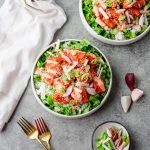 Bowl with chopped romaine lettuce, rice, and gochujang salmon topped with radish and green onions