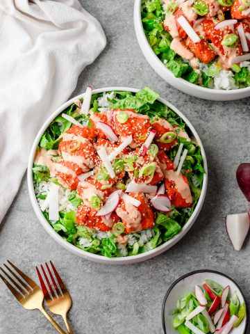 Bowl with chopped romaine lettuce, rice, and gochujang salmon topped with radish and green onions
