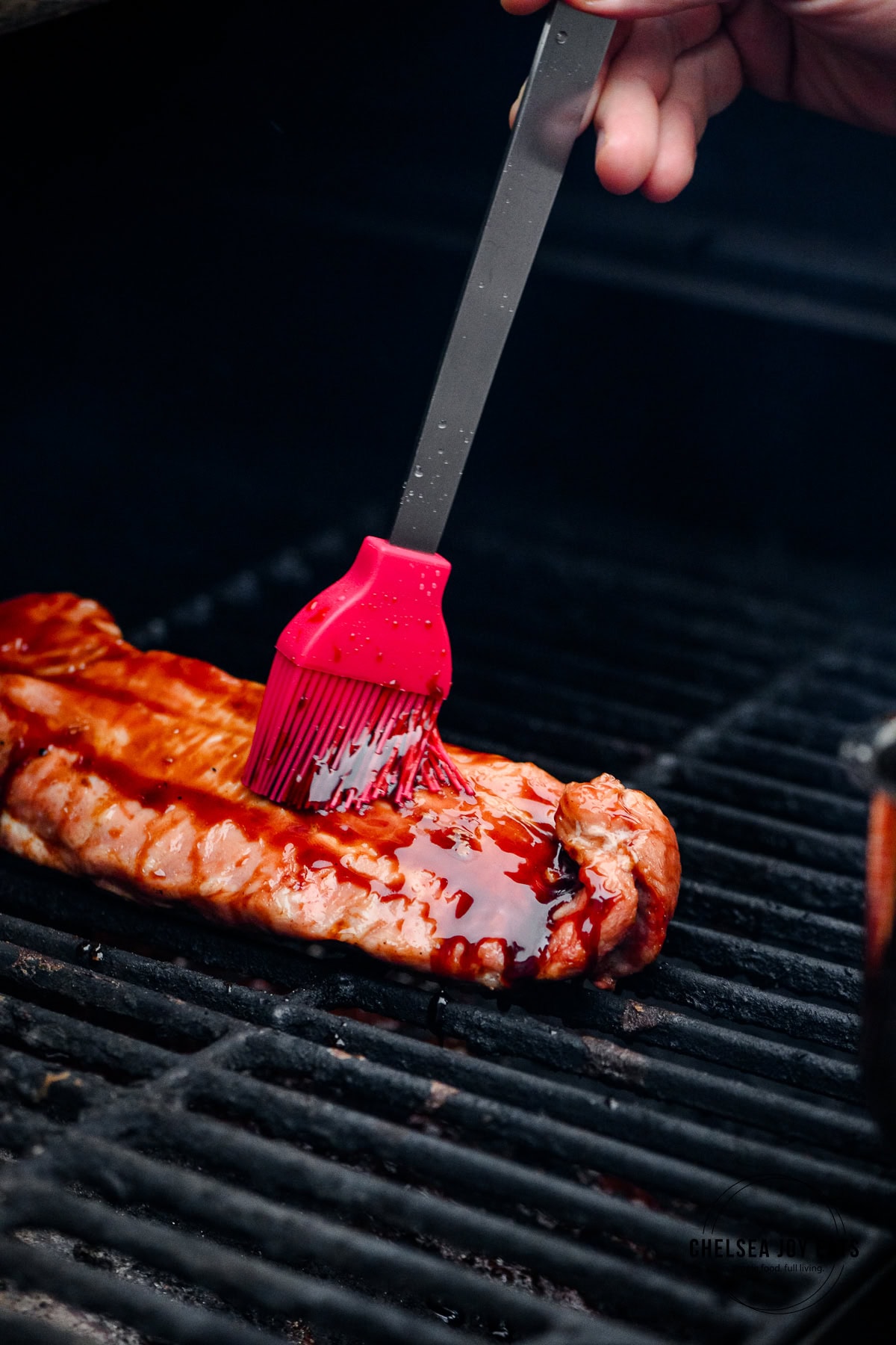 Silicon brush glazing a pork tenderloin with balsamic reduction on the grill