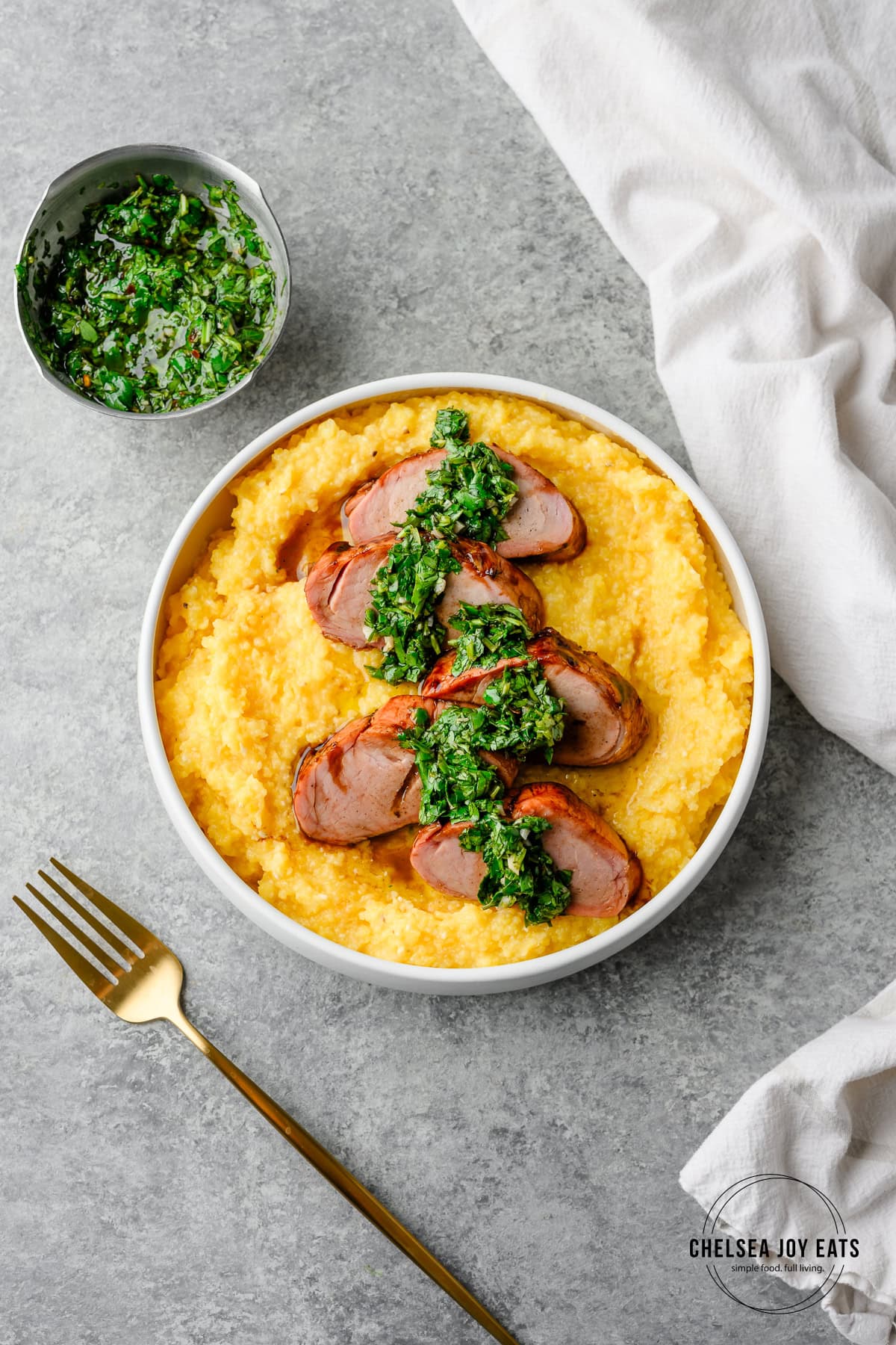 Smoked pork tenderloin served over polenta with chimichurri drizzled overtop, with more chimichurri on the side