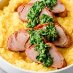 Closeup of smoked balsamic pork tenderloin served over polenta and drizzled with chimichurri