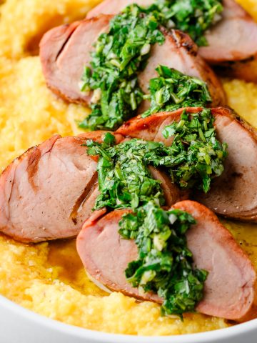 Closeup of smoked balsamic pork tenderloin served over polenta and drizzled with chimichurri