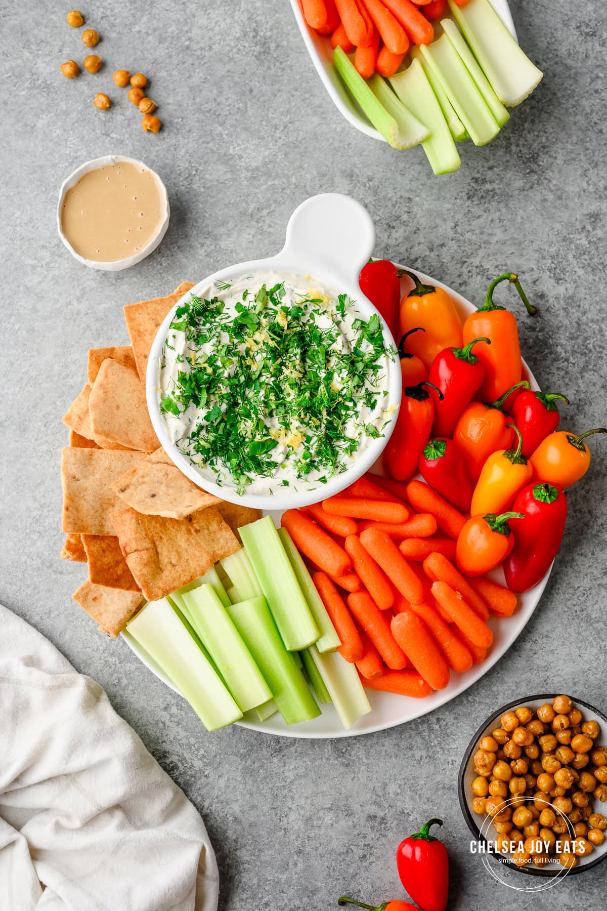 Overhead view of an herby Tahini Yogurt Dip garnished with fresh herbs and surrounded by chips and fresh veggies