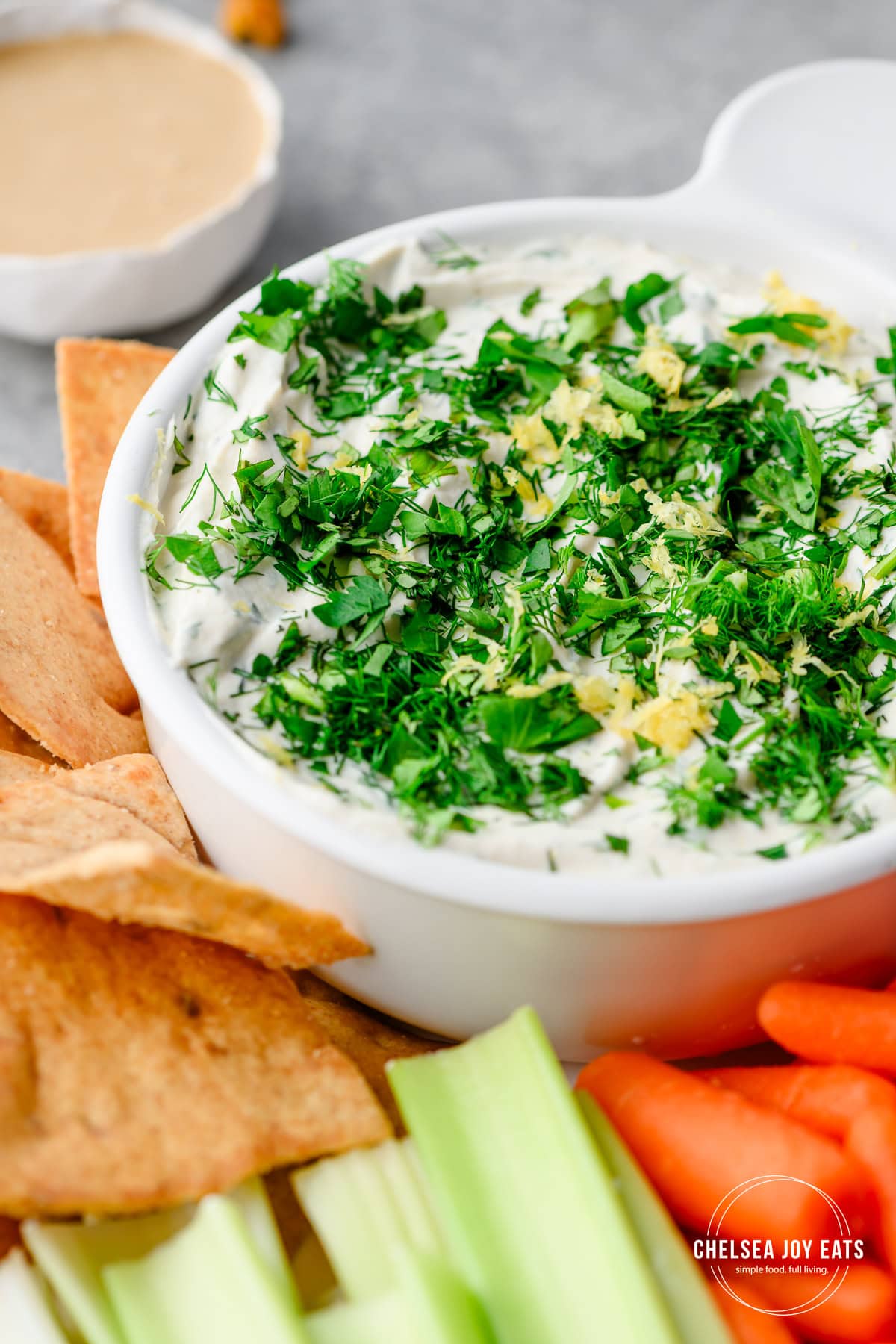 Closeup of a savory veggie dip made with Greek yogurt and tahini and garnished with chopped fresh herbs