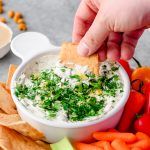 Closeup of Lemon Herb Tahini Yogurt Dip with someone scooping with a chip