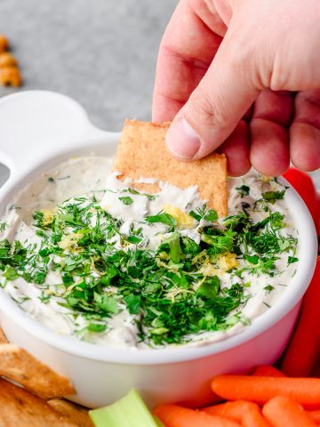 Closeup of Lemon Herb Tahini Yogurt Dip with someone scooping with a chip