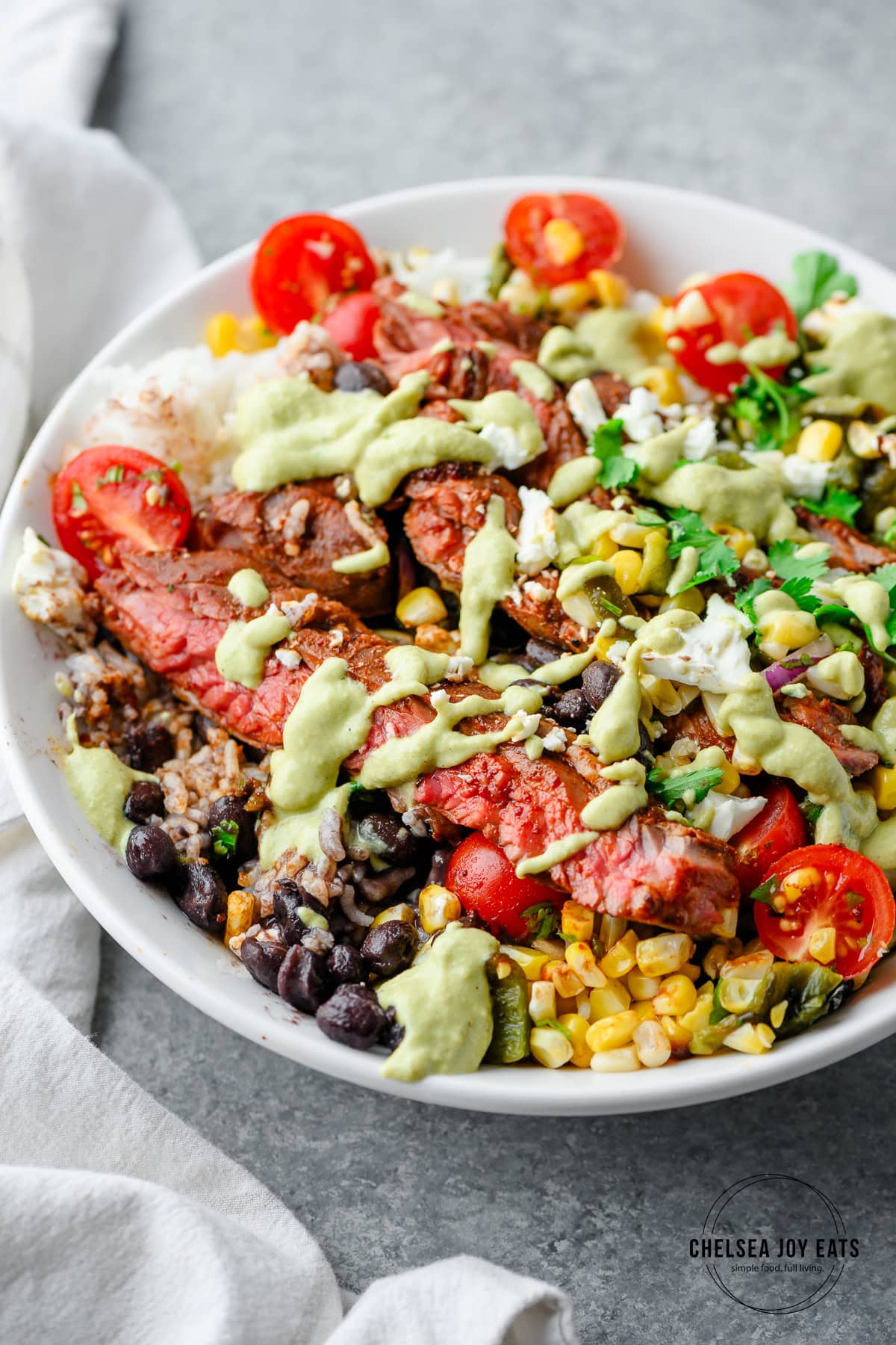 Closeup of a rice bowl with ancho steak, black beans, and poblano corn salsa, drizzled with poblano cream sauce
