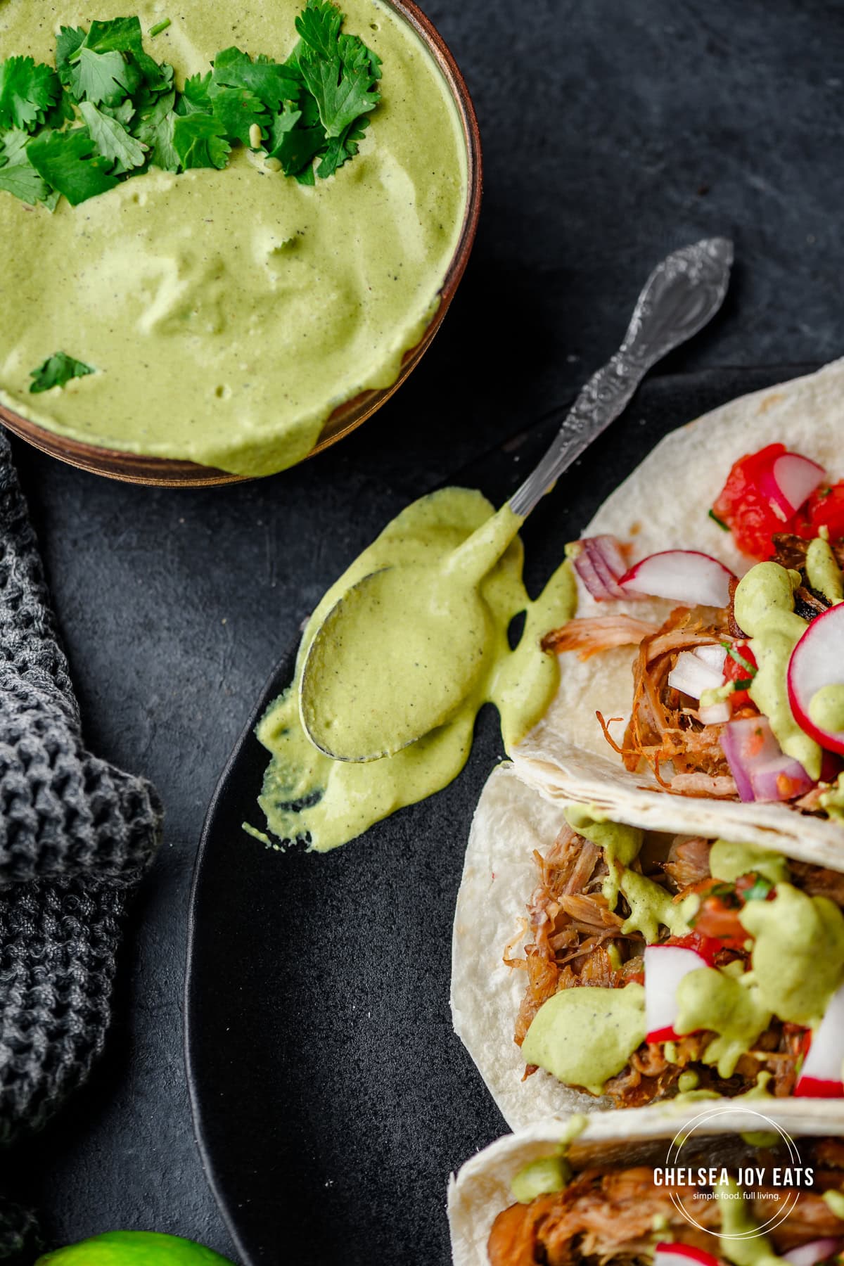 Spoon with poblano sauce on it next to several tacos drizzle with the sauce