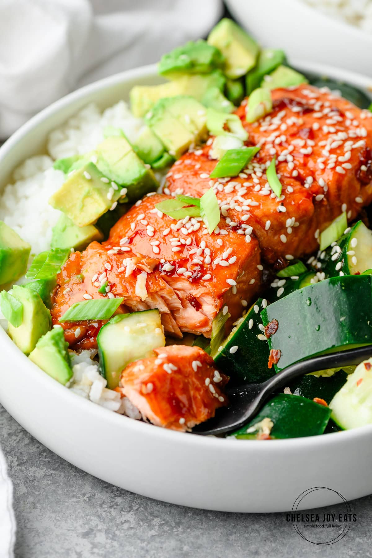 Closeup of a teriyaki salmon bowl with avocado and cucumber salad