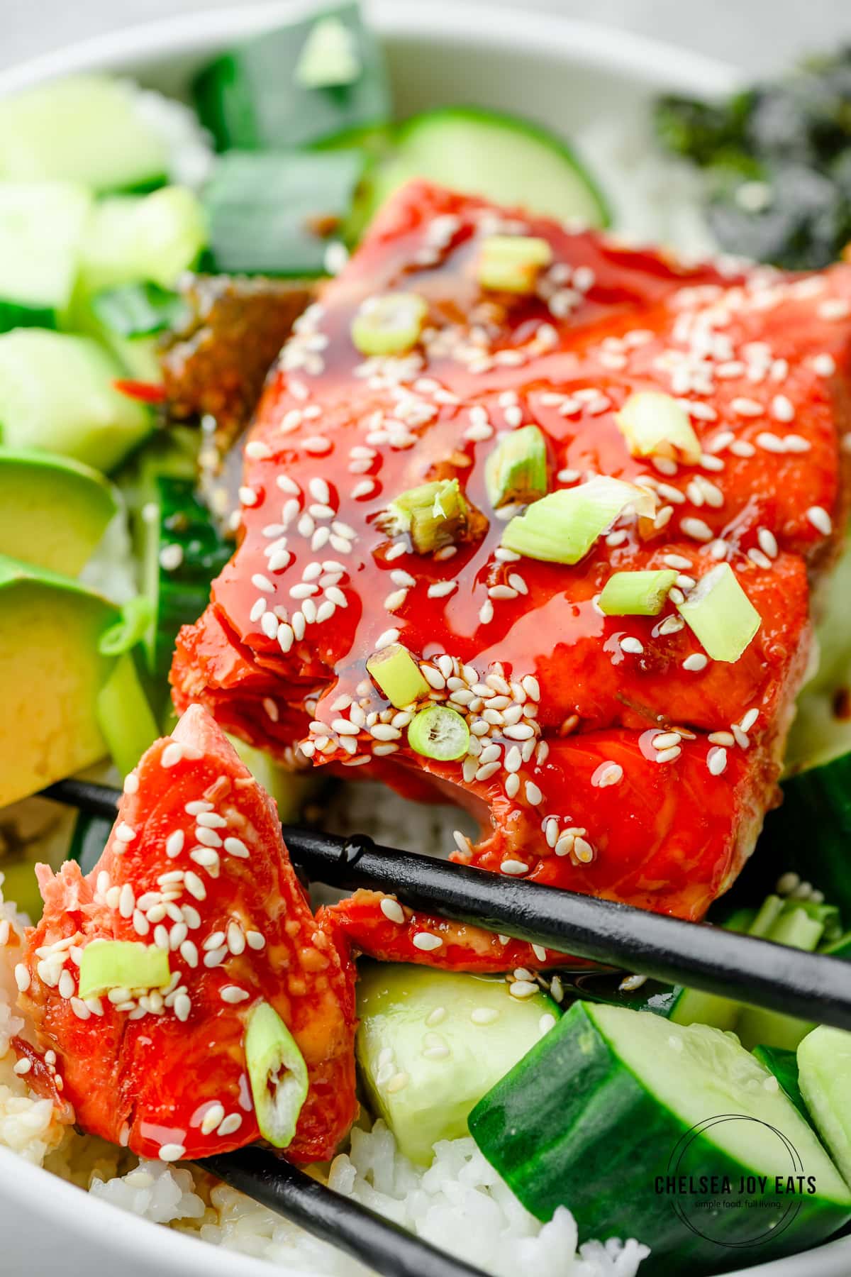 Closeup of a teriyaki salmon fillet over rice with a cucumber salad and sliced avocado