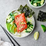Teriyaki salmon and rice bowl served with cucumber salad, sliced avocado, and nori