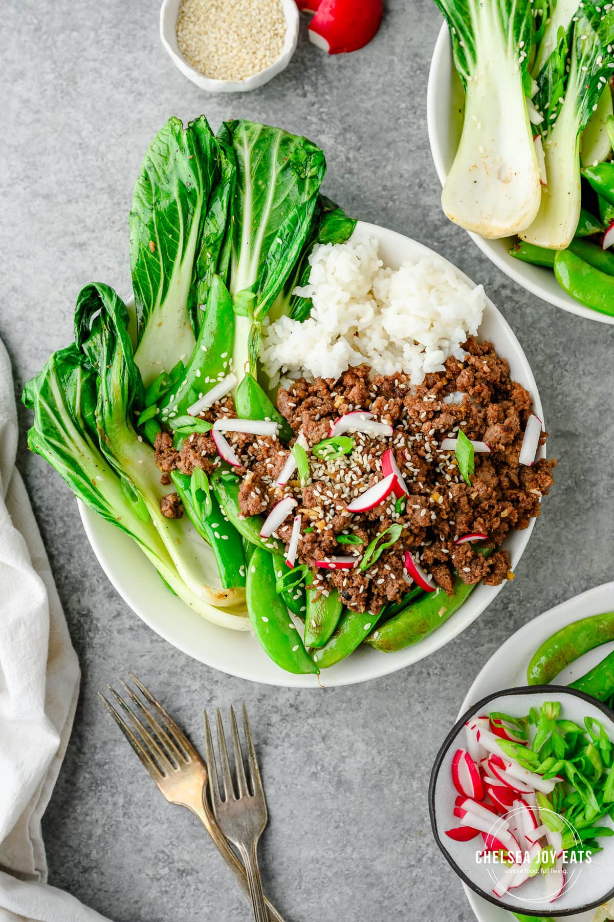 Dinner bowl with ground beef teriyaki, rice, Bok choy, snap peas, and garnished with sesame seeds and radishes