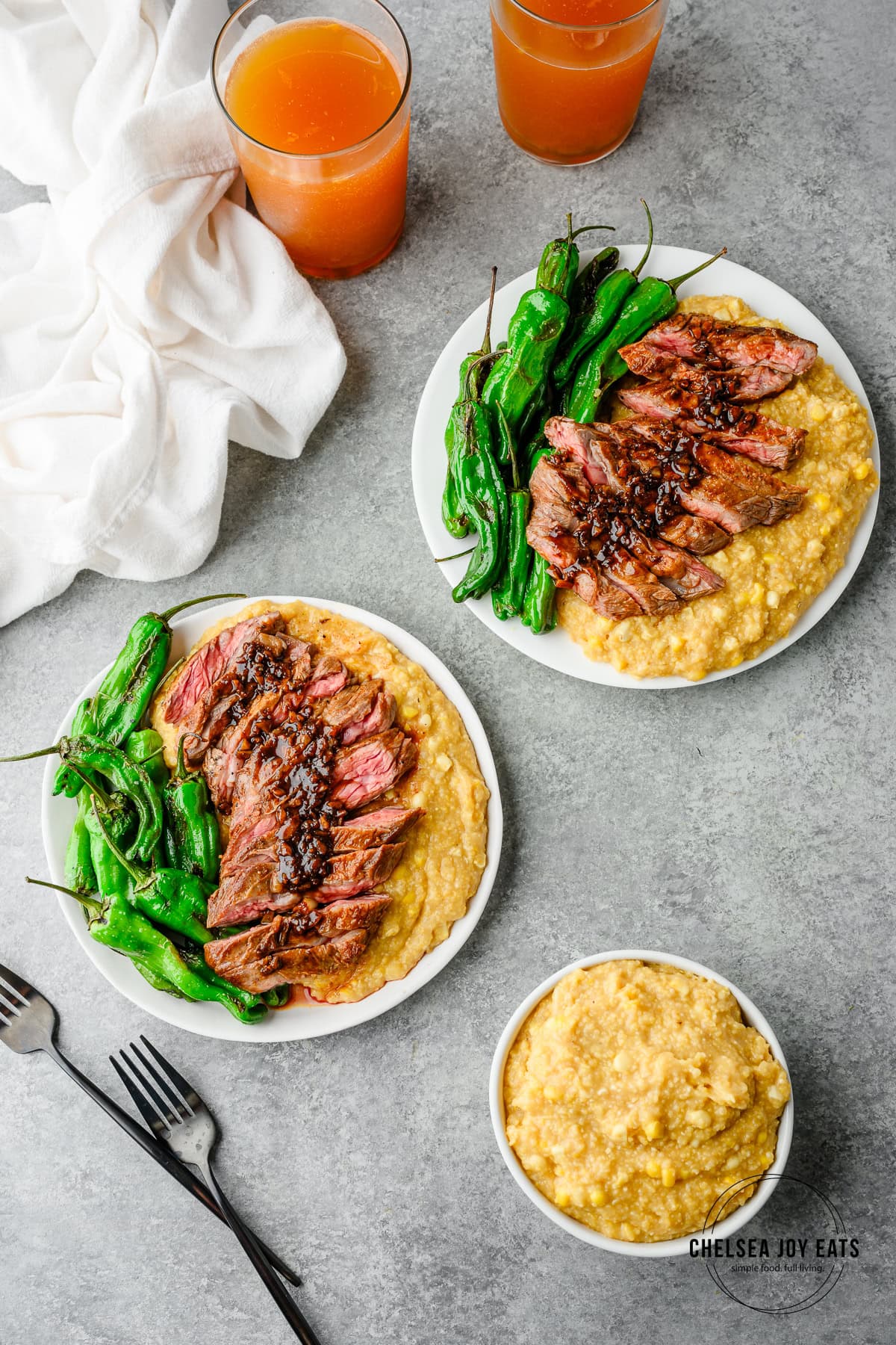 Overhead view of plates serving sliced skirt steak with double-corn polenta and shishito peppers