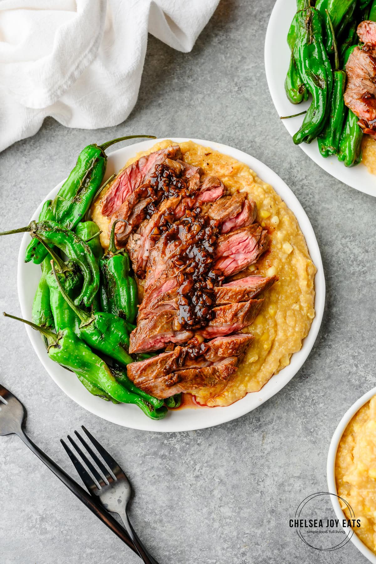 Overhead view of sliced skirt steak served over cooked polenta with extra corn and blistered shishito peppers