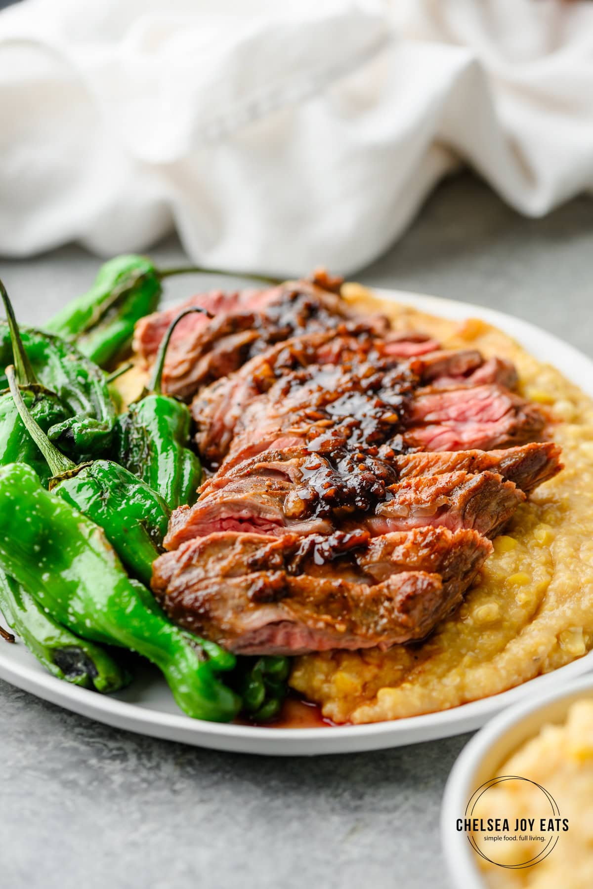 Sliced steak with pan sauce served over double-corn polenta and blistered shishito peppers