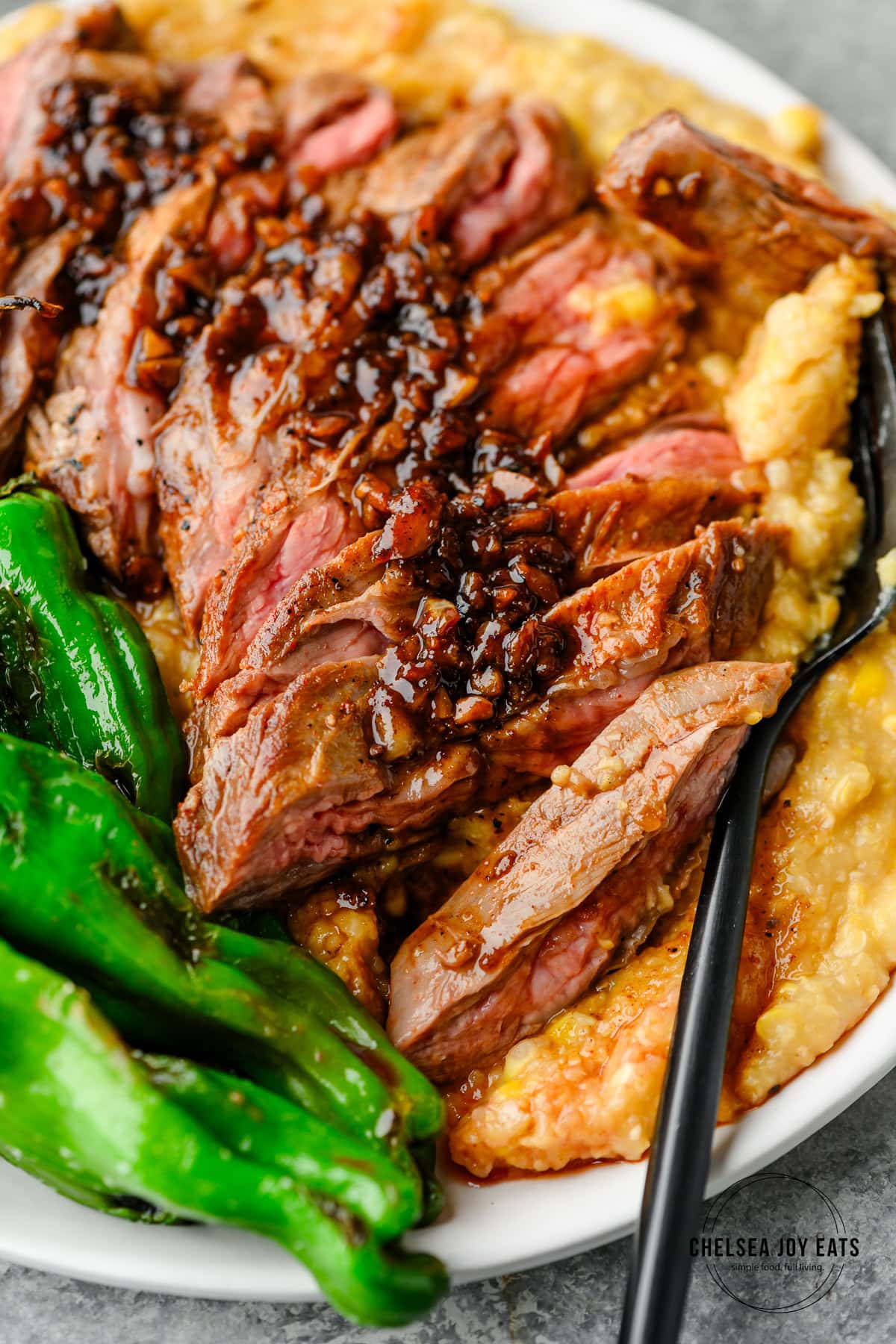 Closeup of sliced skirt steak served over polenta and with shishito peppers and a garlicky pan sauce