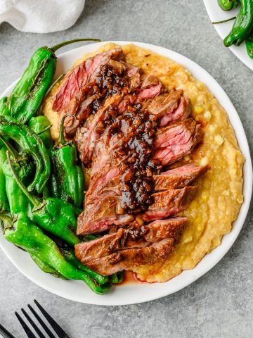 Overhead view of plate loaded with polenta, blistered shishitos, and sliced skirt steak with pan sauce