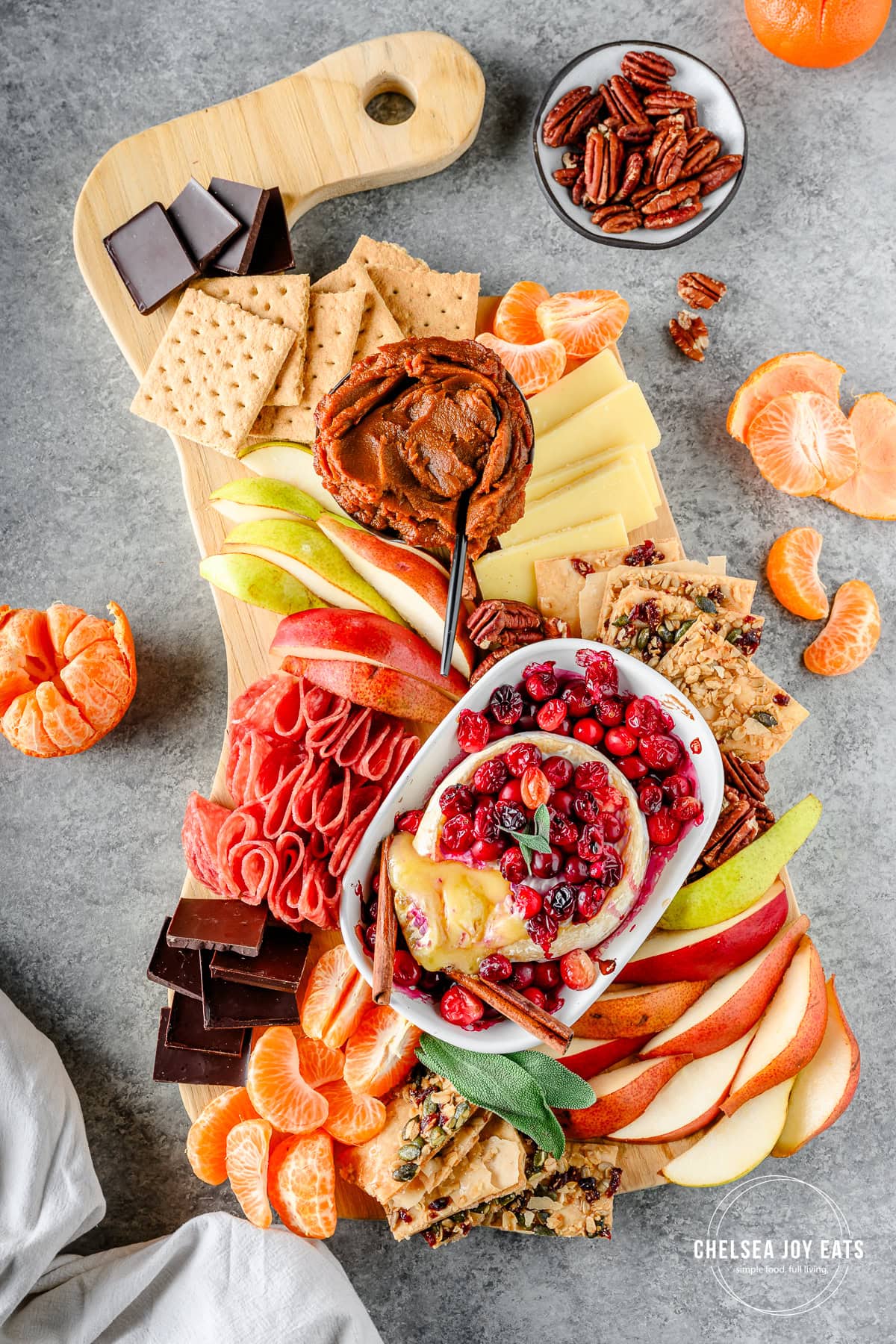 Overhead view of a charcuterie board with fall-inspired flavors, including seasonal produce, pumpkin butter, cranberry baked brie, and more
