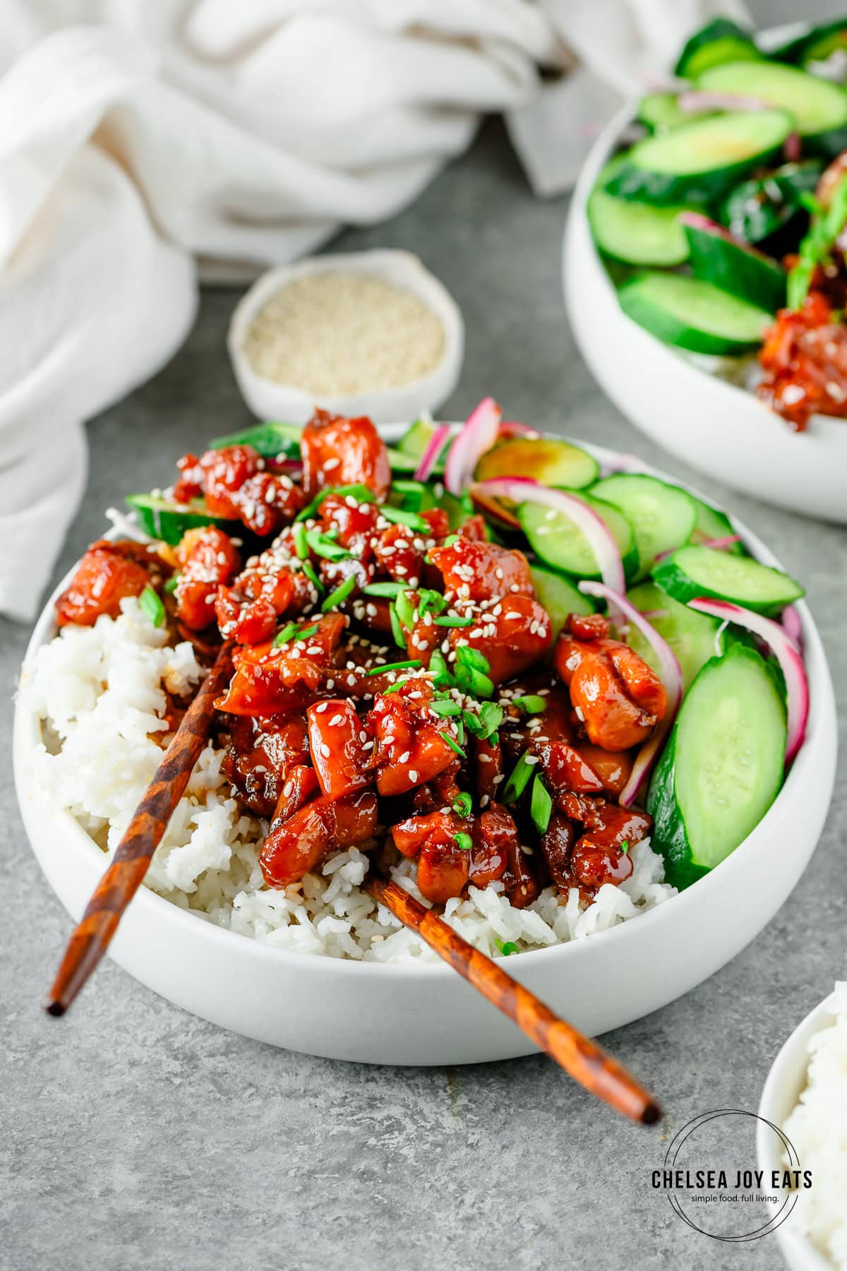 Closeup of a bowl of chicken teriyaki served over rice with marinated cucumbers