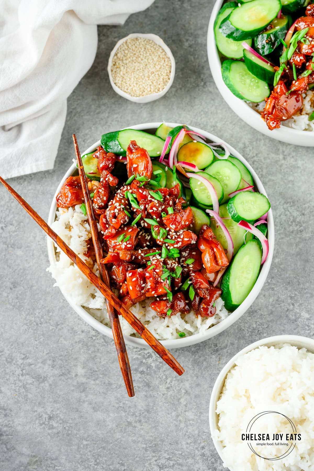 Overhead view of gluten free chicken teriyaki bowls served with cucumbers over rice, with chopsticks alongside