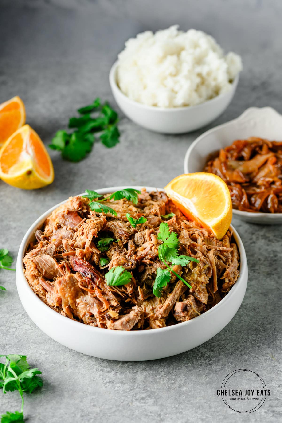 Bowl of Orange Braised Pork Shoulder with bowls of caramelized onions and rice in the background