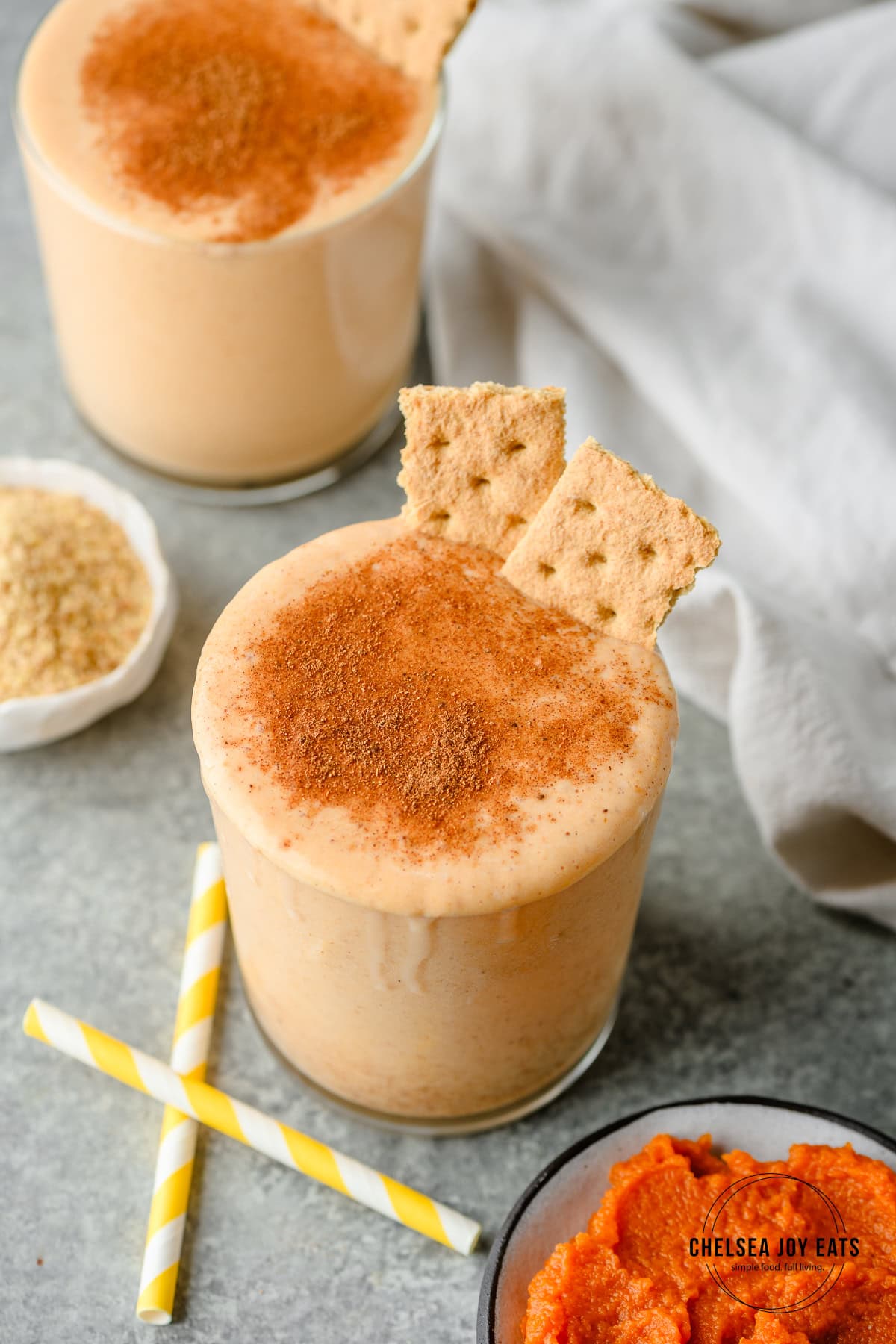 Pumpkin protein smoothie in a small glass, dusted with pumpkin pie spice and garnished with graham crackers