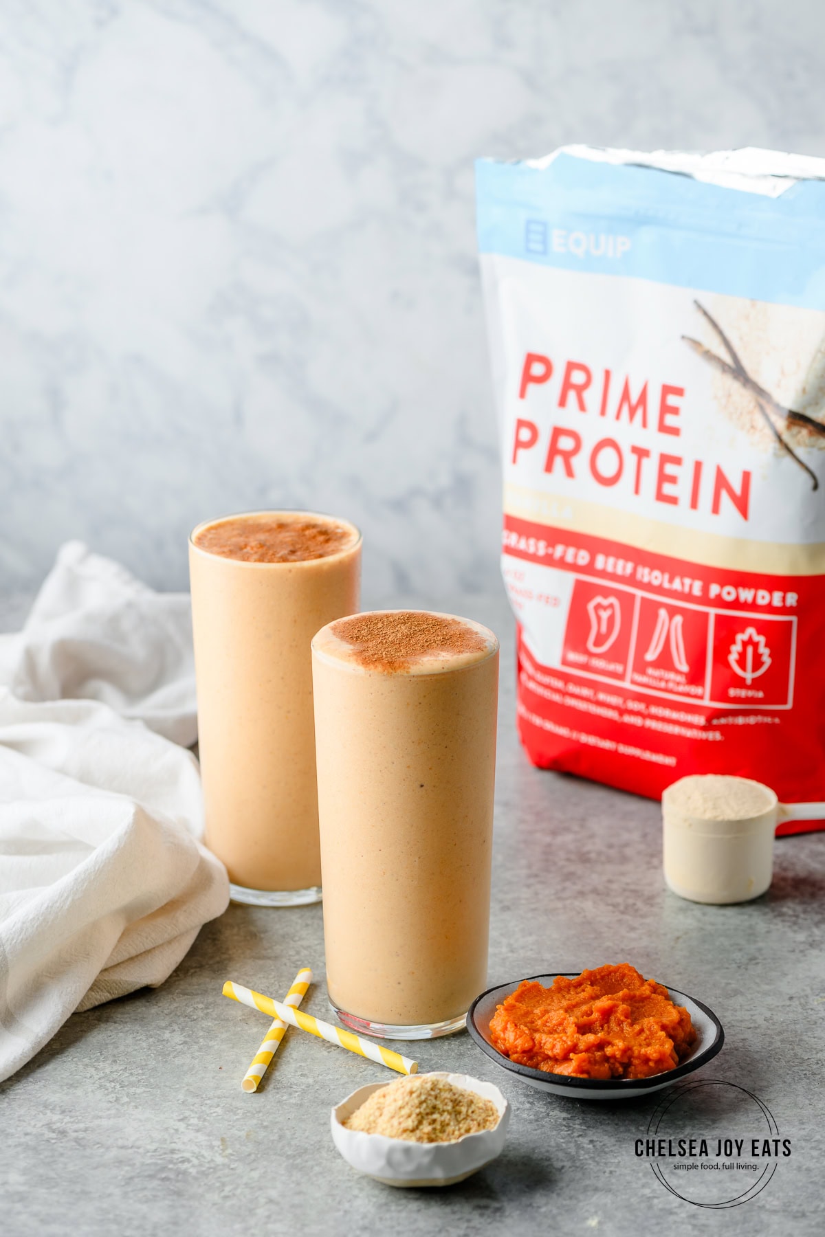Pumpkin protein smoothie with ingredients in dishes in the foreground and background as well as a bag of Equip prime protein, vanilla flavor