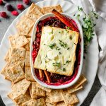 Overhead view of baked feta served over cranberries with crackers beside