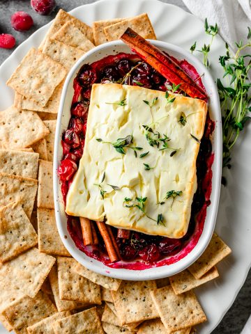 Overhead view of baked feta served over cranberries with crackers beside