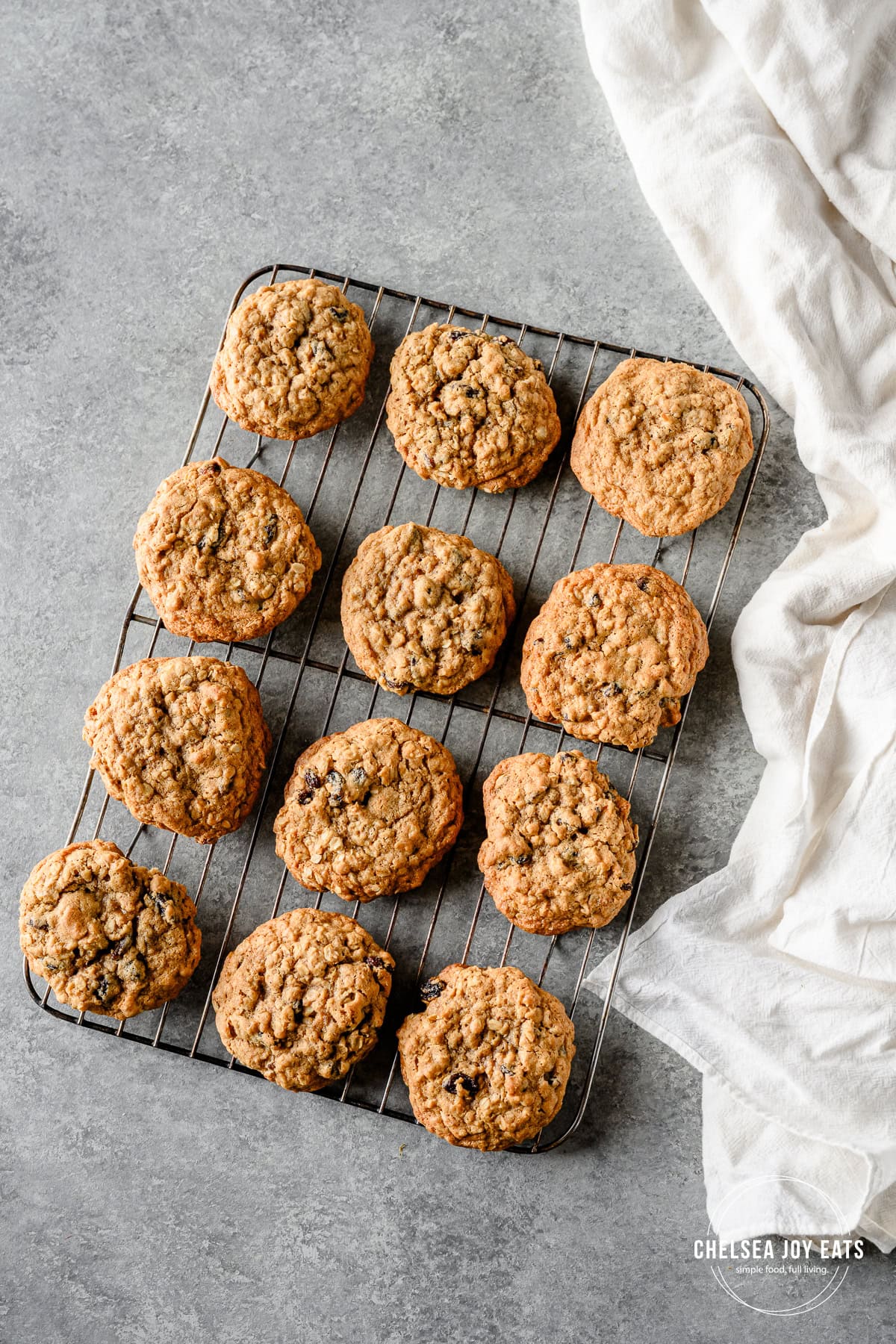 Overhead view of oatmeal raisin cookies cooling on a wire rack, with a white linen alongside