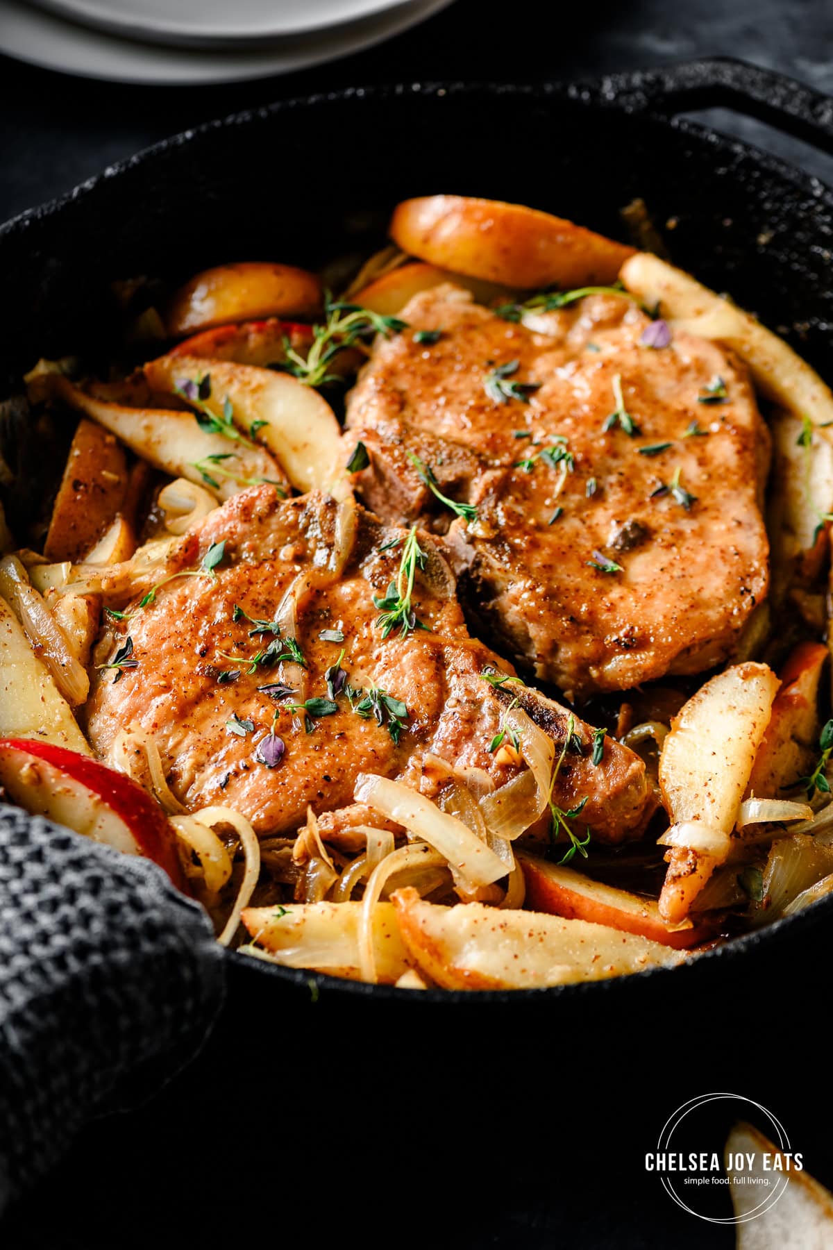 Closeup of cooked pork chops in a skillet with sauteed pears, garnished with thyme