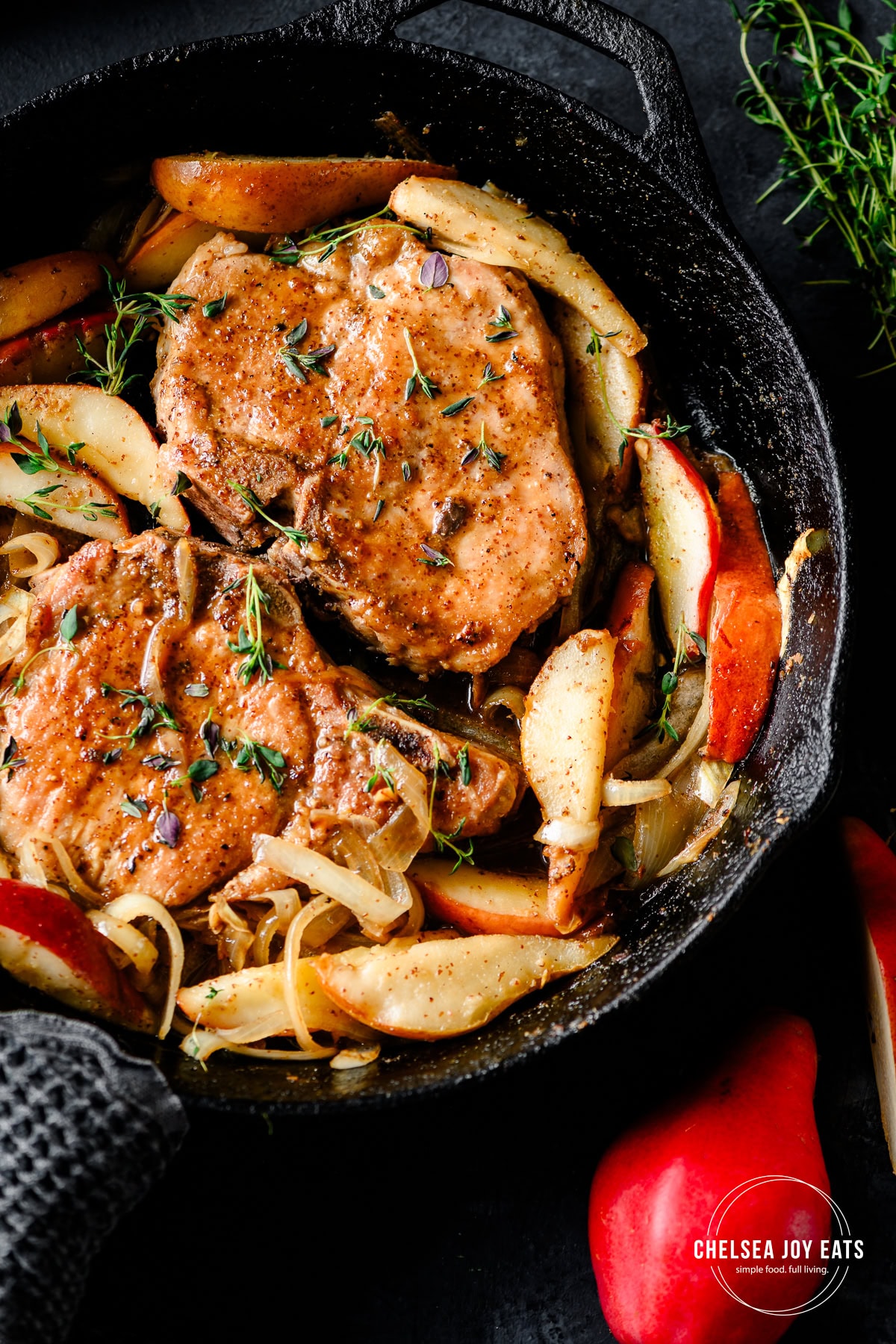 Cooked pork chops with maple-glazed pears in a cast iron skillet, garnished with thyme