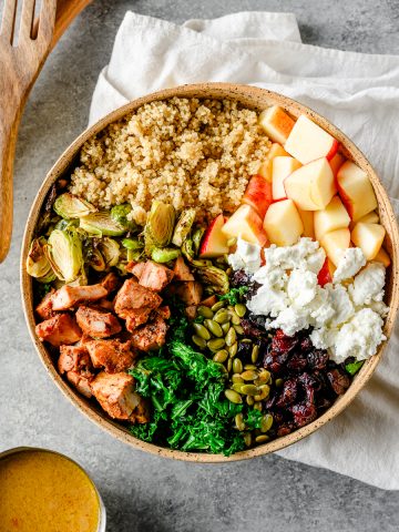 Overhead view of a roasted brussels sprout salad with quinoa and kale divided by ingredients in a bowl