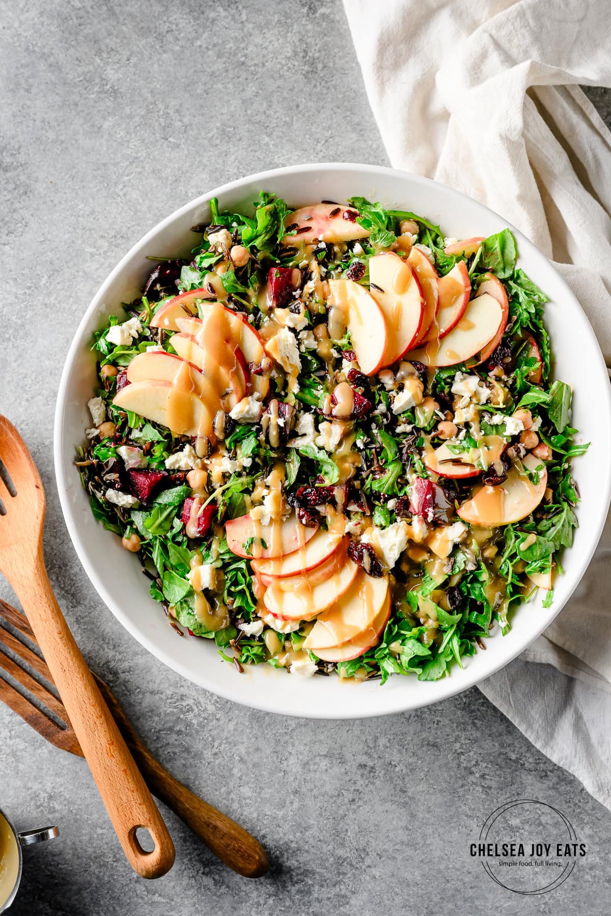 Overhead view of a wild rice and arugula salad topped with sliced apples and drizzled with maple tahini vinaigrette in a large bowl