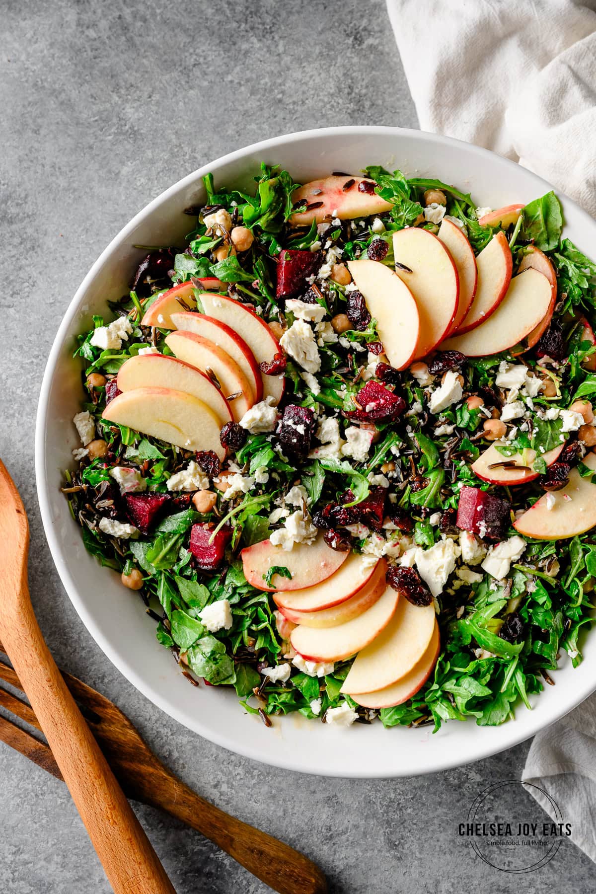 Overhead view of a hearty arugula salad with wild rice, beets, goat cheese, and garbanzo beans, topped with sliced apples