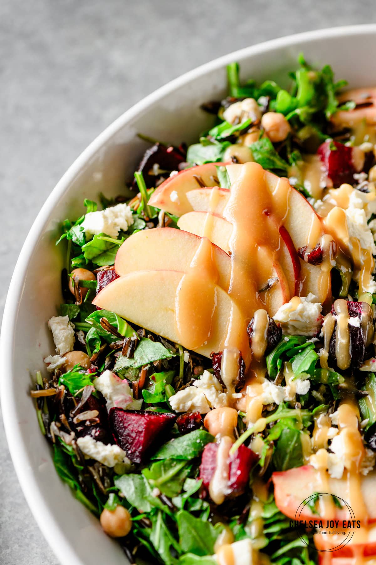 Closeup of sliced apples on an arugula and wild rice salad with beets, feta cheese, and maple tahini vinaigrette